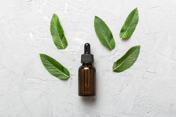 Aceite esencial de menta natural en una botella de vidrio. cosméticos orgánicos con extractos de hierbas de menta sobre fondo de color. - Foto, imagen