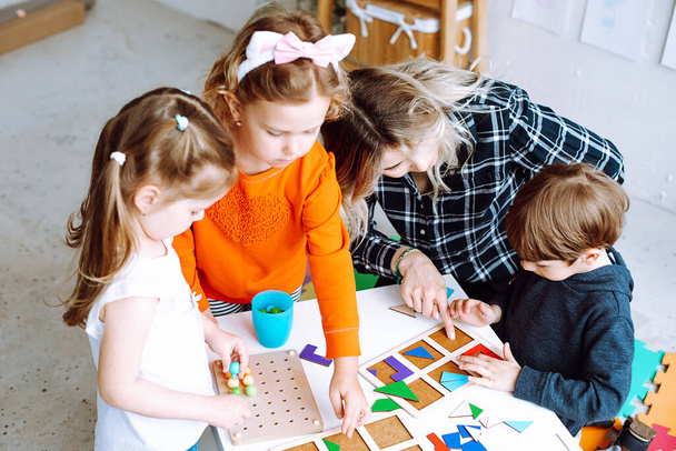 Маленькі діти з педагогом складають барвисті деталі конструктора на столі в ігровій кімнаті зверху. Цікава гра для дитячих садочків, що розвивають логіку та інтелект. Спілкування з однолітками
. - Фото, зображення