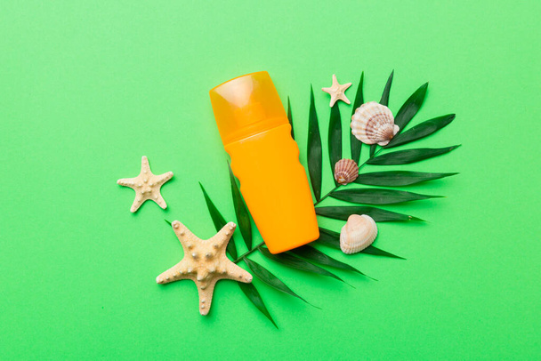 Sunscreen spray bottle. Bottle with sun protection cream and sea shells with tropical green leaf on color background, top view. - Fotó, kép
