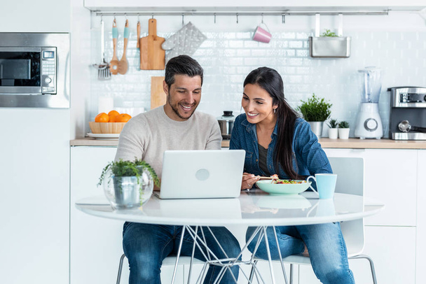 Shot of beautiful lovely couple using their laptop to searching voyage while eating poke bowl in the kitchen at home. - Foto, Imagem