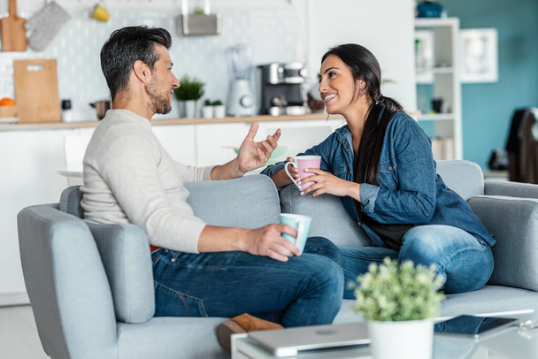 Shot of lovely couple holding coffee cups while talking sitting on couch at home. - Foto, Bild