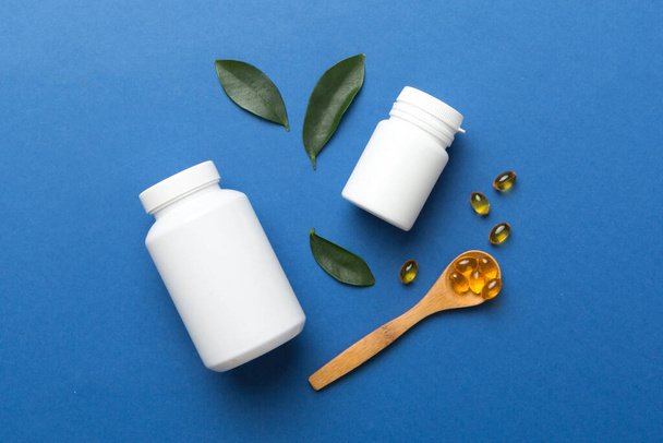 Omega-3 kapselit ovat valkoisessa pullossa pöydällä vihreät lehdet tausta. Kalaöljytabletit. Biologisesti aktiiviset lisäaineet. omega 6, omega 9, A-vitamiini, E, D, D3-vitamiini ylhäältä katsottuna kopiotilaa. - Valokuva, kuva