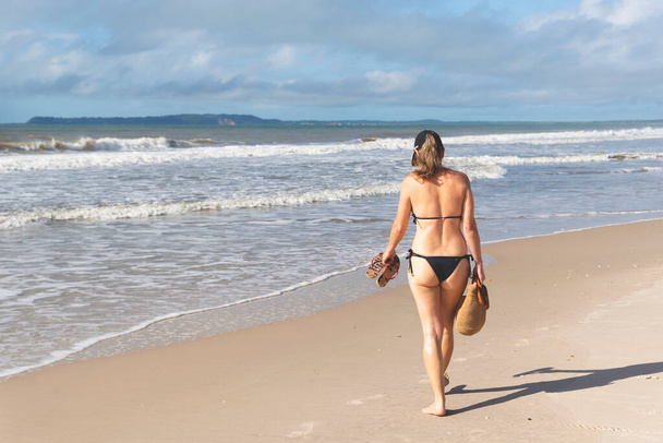 Kobieta w bikini spacerująca po plaży z piaskiem na tle błękitnego nieba. Walencja, Bahia, Brazylia. - Zdjęcie, obraz