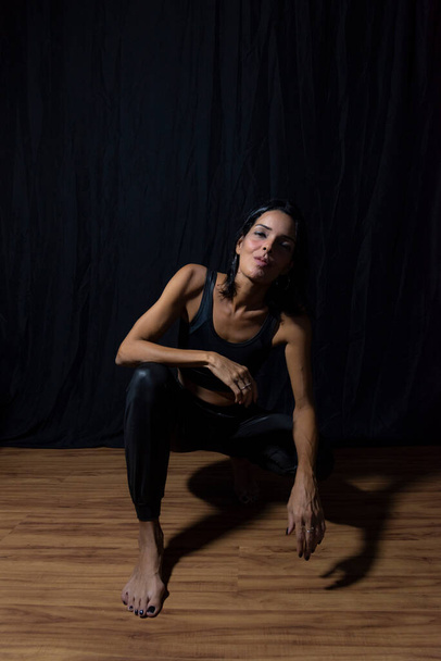 黒を背景に床に座っている女性の肖像画。サルバドール,バイーア,ブラジル. - 写真・画像