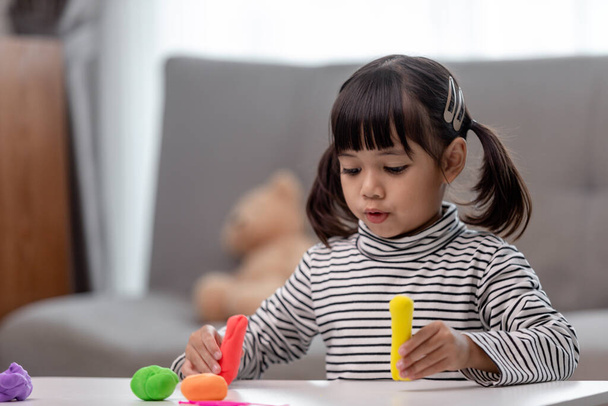 Het kleine meisje leert kleurrijk speeldeeg te gebruiken in een goed verlichte kamer  - Foto, afbeelding