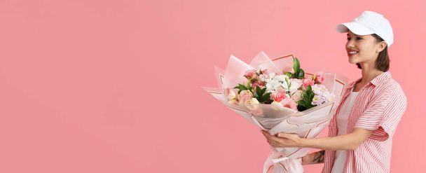 Female courier with bouquet of flowers on pink background with space for text - Foto, Imagem