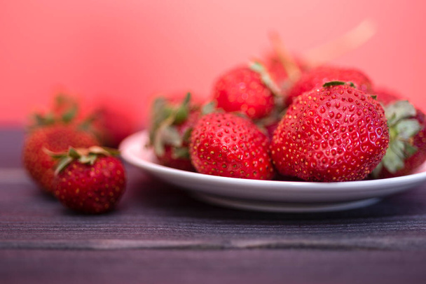 Fresh strawberries in a white plate on a dark wooden background. The concept of fresh and healthy food. copy space. - Foto, imagen