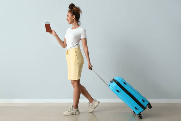 Turista afro-americana con passaporto e valigia vicino alla parete luminosa - Foto, immagini