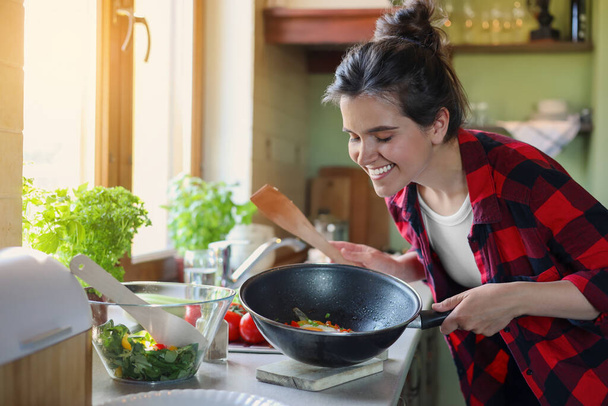 Young woman holding pan with freshly fried eggs and vegetables in kitchen - Photo, Image
