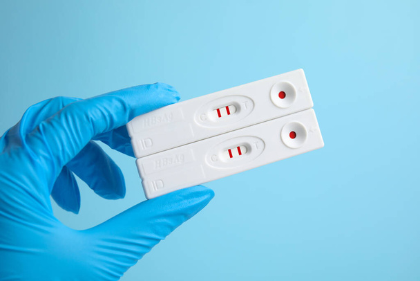 Doctor holding two disposable express tests for hepatitis on light blue background, closeup - 写真・画像