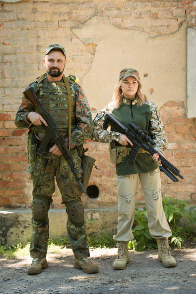 Man and woman, Ukrainian defenders with weapons near the destroyed building during the war in Ukraine - 写真・画像