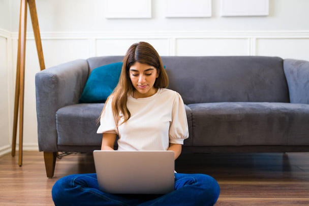 Atrakcyjna kobieta pisząca na laptopie i dojeżdżająca do pracy podczas pracy na własny rachunek w swoim salonie  - Zdjęcie, obraz