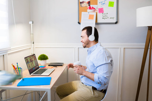 Profilo di un uomo allegro con le cuffie che sorride alla scrivania durante una videochiamata online mentre lavora da casa - Foto, immagini