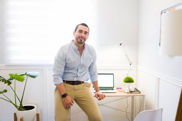 Attractive happy man leaning on his office desk while working remotely and finishing his professional work - Photo, Image