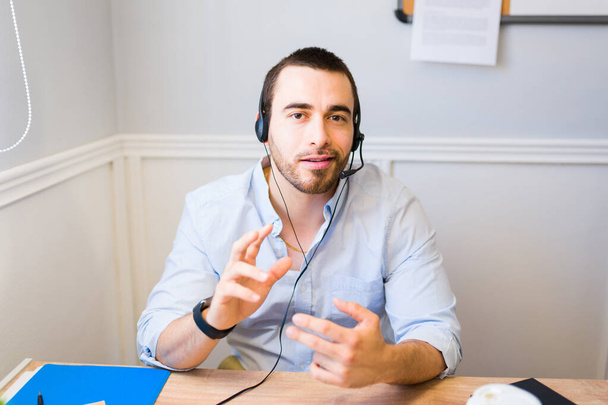 Retrato de un joven caucásico o representante de ventas con un auricular mirando a la cámara y hablando durante una videollamada de trabajo - Foto, Imagen