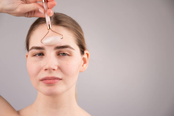 Close-up portrait of a woman uses a quartz roller massager to smooth wrinkles on her forehead - Foto, Imagem