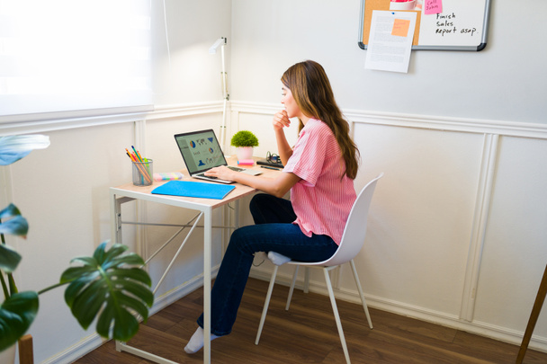 Young woman seen from behind wearing casual clothes and doing freelance work while working remotely from hom - Fotoğraf, Görsel