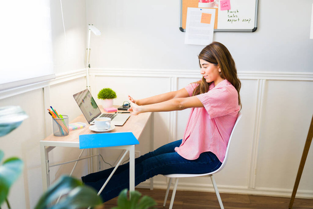 Beautiful hispanic woman stretching her body after sitting in her desk to start her freelance work at home  - Fotoğraf, Görsel