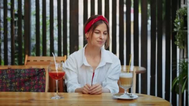 szczęśliwa dziewczyna w kawiarni wybiera, co pić, kawa lub koktajl. letni styl życia i radość - Materiał filmowy, wideo