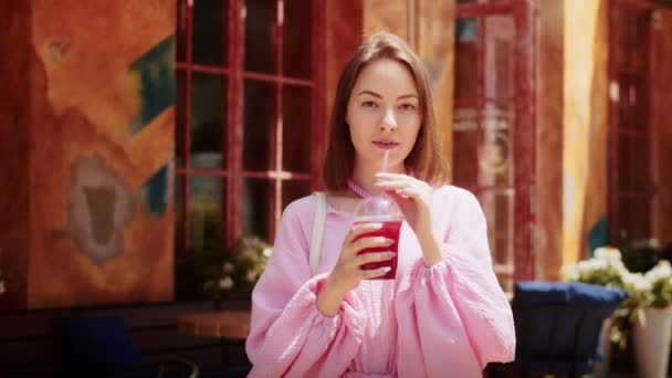 glückliches Mädchen in rosa Kleid trinkt einen Cocktail auf der Straße vor dem Hintergrund des Gebäudes, führt einen lockeren Lebensstil und hat Spaß im Sommer - Filmmaterial, Video