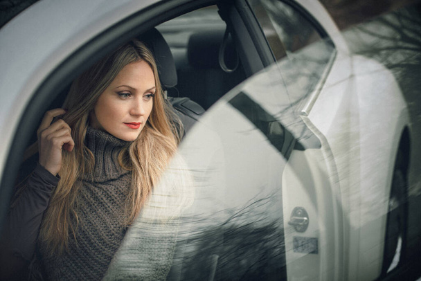 Une œuvre d'art. Une photo d'une belle fille élégante assise dans une voiture. Il y a de belles reflets sur les fenêtres de la voiture. - Photo, image