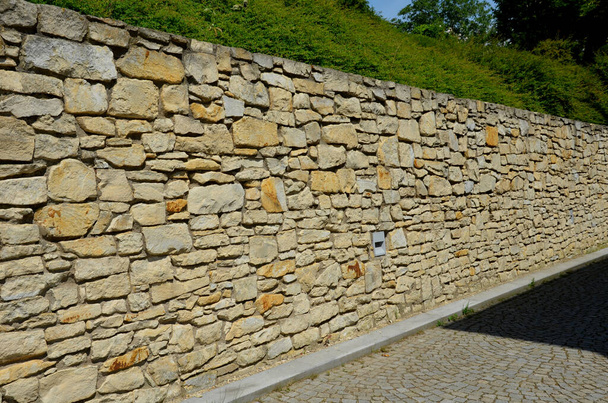 beautifully folded retaining wall with a granite attic with small joints. brown beige yellow irregular gneiss stone holding a slope above it. there are undemanding perennials around - Φωτογραφία, εικόνα