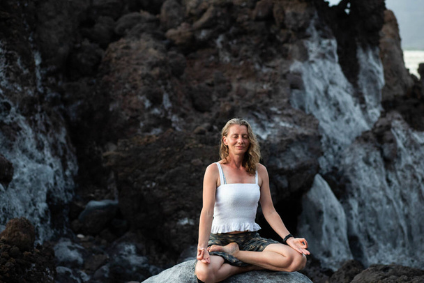 красива жінка сидить в медитації проти темних скель
  - Фото, зображення