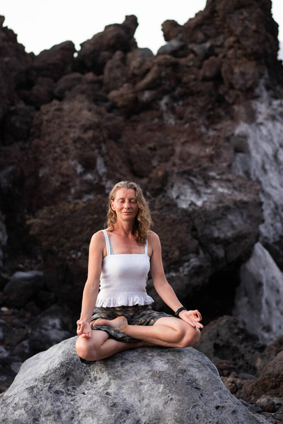 beautiful woman sitting in meditation against dark rocks  - 写真・画像