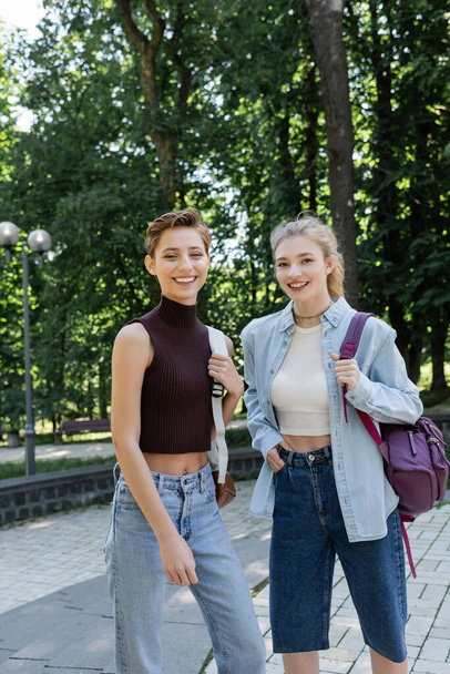 Cheerful students with backpacks looking at camera in park  - Foto, imagen