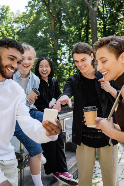 Multiethnic students with coffee to go looking at cellphone in park  - Fotoğraf, Görsel