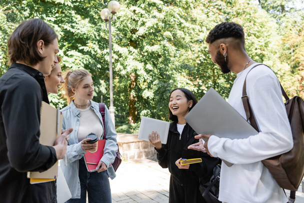 Asian student holding digital tablet near smiling multiethnic friends in summer park  - Valokuva, kuva