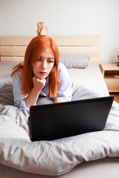 bored young woman lying on bed with laptop computer - Photo, image