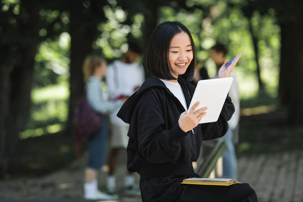 Positive asian student having video call on digital tablet in park  - Foto, Bild