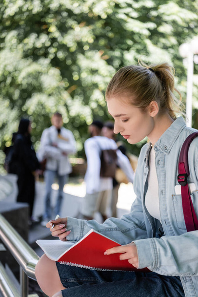 Вид сбоку на студента с ручкой и копировальной книгой в парке  - Фото, изображение