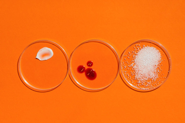 Kosmetické hodinky. Vzhled textury smetany, červené masky a granulí v Petriho miskách na oranžovém pozadí. Přírodní produkty pro péči o pleť. Koncept krásy pro péči o obličej a tělo - Fotografie, Obrázek