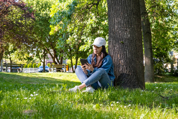 donna seduta sotto l'albero che legge lo spazio elettronico della copia del libro - Foto, immagini