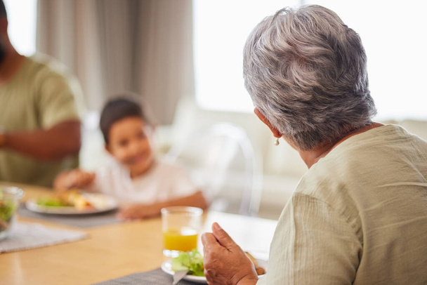 Widok z tyłu zbliżenie dojrzałej mieszane rasy kobieta jedząc lunch z rodziną przy stole w salonie w domu. - Zdjęcie, obraz