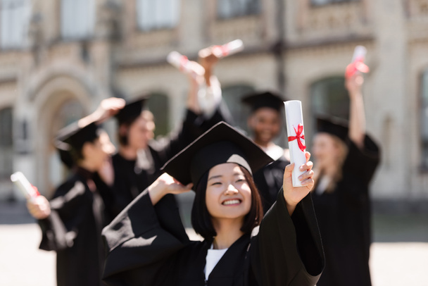 Felice scapolo asiatico in cap holding diploma all'aperto  - Foto, immagini