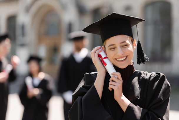 Веселий холостяк у кепці, що тримає диплом біля обличчя на відкритому повітрі
  - Фото, зображення
