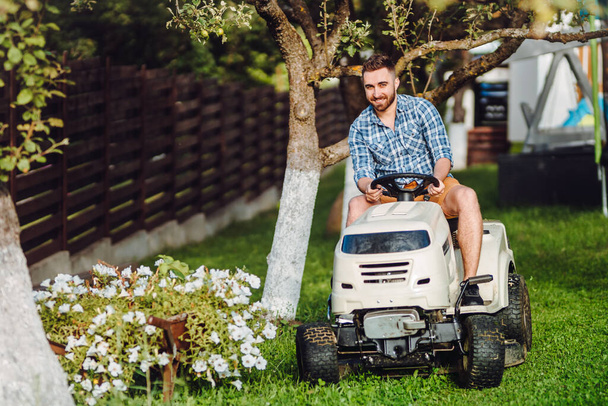 Professional gardener and lawn mower cuts the grass using tracto - Foto, afbeelding