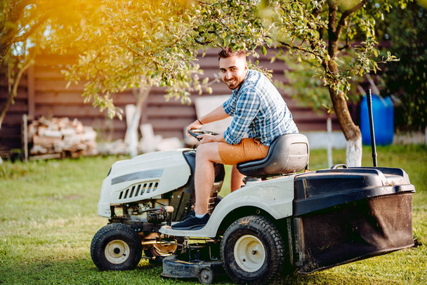 Profesyonel çim biçme makinesi çimleri biçer. Gardda çalışan gülümseyen bahçıvan. - Fotoğraf, Görsel