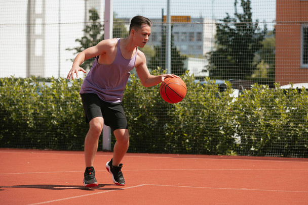 young guy plays basketball on the basketball court. throws the ball into the ring. doing sports. healthy body and healthy lifestyle - Фото, зображення