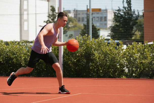 Ο νεαρός παίζει μπάσκετ στο γήπεδο. Ρίχνει την μπάλα στο ρινγκ. κάνοντας αθλήματα. υγιές σώμα και υγιεινό τρόπο ζωής - Φωτογραφία, εικόνα