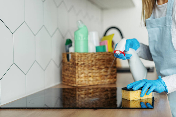 Kobieta w gumowych rękawiczkach czysta szklana powierzchnia ceramiczna na kuchence indukcyjnej, polska kuchnia z gąbką, przy użyciu ekologicznego sprayu. Gospodyni domowa robi codzienną rutynę. Koncepcja usług sprzątania - Zdjęcie, obraz
