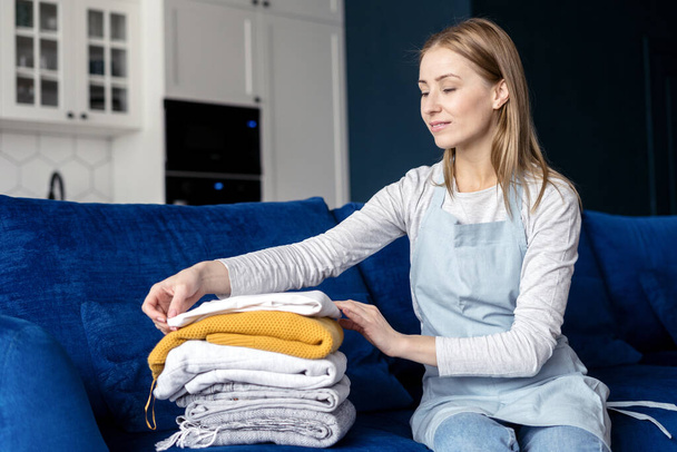 Side view of lady in apron puts things. Process of cleanup pile stack clothes. Housework duties. Housewife concept. Cleaning service worker occupation - Foto, Imagen