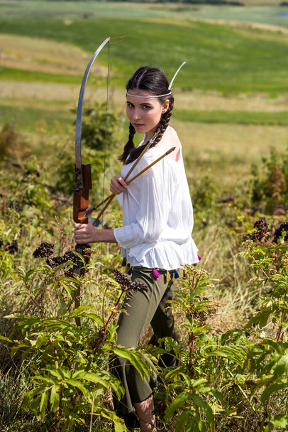  mujer india posa en una naturaleza rodeada de flecha y arco. retrato de cazadora  - Foto, imagen