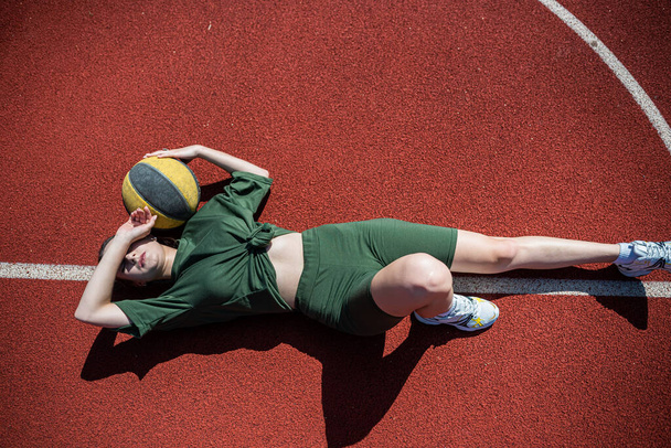 charmante jonge vrouw dragen sport doek met een basketbal is rusten na een training. actieve zomerdag voor sport - Foto, afbeelding