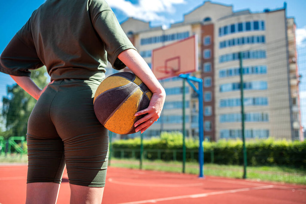 atletisch meisje gooit een basketbal in de mand, speelt alleen, traint buiten. sport voor de gezondheid - Foto, afbeelding
