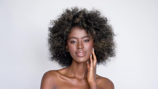 Belle femme africaine ethnique avec des cheveux afro bouclés souriant et regardant la caméra sur fond gris - Séquence, vidéo
