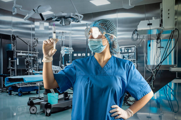 female doctor or assistant wear blue uniform with gloves,  face mask glasses and hat for full protection from virus holding syringe with medication in surgery room  - Φωτογραφία, εικόνα